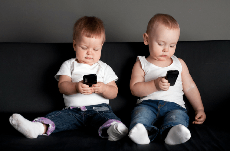 Teknolojinin Çocuk Gelişimine Etkisi başlıklı makalede kullanılan, cep telefonuyla oynayan iki çocuğun bir koltukta otururken çekilmiş fotoğrafı